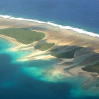 World apart: One of countless islets any flight goes over; the town hall in Majuro serving Bikini Atoll\'s radiation-displaced populace; and Marshallese women in traditional muumuu dresses. | CHRISTOPHER JOHNSON