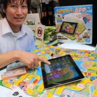 New meets old: An employee of Takara Tomy shows off the prototype Jinsei Game APP for the iPad, which goes with the venerable board game, during the International Tokyo Toy Show 2012 at Tokyo Big Sight on Thursday. | SATOKO KAWASAKI