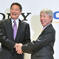 Common cause: Sony Corp. President Kazuo Hirai (left) shakes hands with Olympus Corp. President Hiroyuki Sasa after their news conference in Tokyo on Monday. Olympus and Sony announced that they have entered into business and capital alliance agreements through a third-party allotment to Sony of Olympus\' common shares. | AFP-JIJI