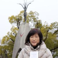 Never forget: Keiko Miyamoto holds up an English translation of \"Memories of Sadako\" at the Hiroshima Peace Memorial Park recently. | KYODO PHOTO