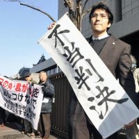 It\'s not over: A lawyer holds a sign that reads \"unjust decision\" Friday after the Tokyo High Court ruled the metropolitan government was not in the wrong for ordering his clients &#8212; teachers and other high school staff &#8212; from observing the national anthem and flag in school ceremonies. | KYODO PHOTO