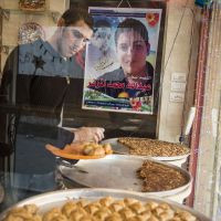Still near: Sami Badawi puts out baklava pastries under the gaze of his deceased friend, Abdullah Muzannar, who is featured on a poster at the Jabalya refugee camp sweet shop where they worked together. | THE WASHINGTON POST