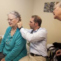 Quality metrics: Physician assistant Keith Bell, of Mosaic Medical in Bend, Oregon, examines Marilyn Gribble, accompanied by her daughter, Deborah Gribble. Oregon\'s health care plan has focused on making high-quality care less expensive. Integrating systems, such as physical, dental and mental health, is part of the approach. | WASHINGTON POST