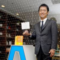 Head coach: Yoshiyuki Suzuki, president of Coach A Co., holds one of his books on corporate coaching while standing in front of his office in Chiyoda Ward, Tokyo, last month. | YOSHIAKI MIURA PHOTO