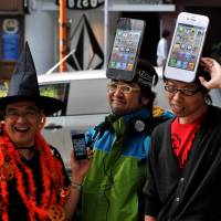 Dialed in: People line up with hats modeled after the new iPhone 4S handset in front of Softbank\'s flagship shop in Tokyo\'s Omotesando district Friday morning. | YOSHIAKI MIURA