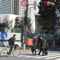 Failure to yield: A bicyclist ignores a red light at an intersection as pedestrians use a crosswalk Thursday in the Shibaura district in Minato Ward, Tokyo. Cyclists who flout law face charges