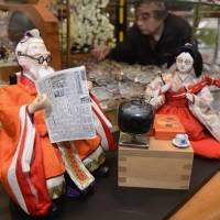 All dolled up: A pair of Hina dolls wearing glasses and relaxing in front of a television are displayed in the front of a Gujo, Gifu Prefecture, eyewear shop earlier this month. | KYODO