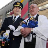 Beyond steam: In railway garb, Mayor Chozo Nakagawa of Kasai, Hyogo Prefecture, holds bottles of biodiesel for a train Saturday at the city\'s Hojomachi Station, in the presence of two baby monkey \"stationmasters.\" | KYODO PHOTO