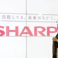 Eye to eye: A woman passes a liquid crystal display monitor showing the Sharp Corp. logo in Tokyo on Aug. 2. The catchline says: \"We are aiming for a different future.\" | BLOOMBERG