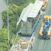 Workers gather scattered bottled detergent Thursday morning after a truck hit a guardrail and spilled its load on the Tomei Expressway in Nakai, Kanagawa Prefecture. | KYODO PHOTO