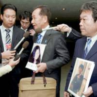 Shigeo Iizuka, whose younger sister, Yaeko Taguchi, was abducted to North Korea in 1978, fields questions from reporters as Teruaki Masumoto, chief secretariat of a group of relatives of abductees, stands by holding a photo of his own missing sister, Rumiko. | KYODO PHOTO
