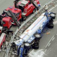 A truck carrying 11 tons of liquefied petroleum gas lies on its side Tuesday morning near a tollgate on the Tomei Expressway in Machida, western Tokyo. The driver was killed in the crash. | KYODO PHOTO