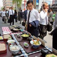 A man looks over samples of lunch specials in front of a restaurant in Tokyo on Thursday as a man using his cell phone passes by. | AP PHOTO