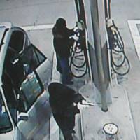 How it went down: Two men wearing black ski masks, with one holding what appears to be a gun and the other trying to break a cash box at a self-service pump, are captured by a security camera early Friday at a gas station in Saitama. | KYODO PHOTO