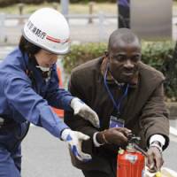 Firefighting 101: A man tries out a fire extinguisher Tuesday during an earthquake drill held for foreign residents in Shibuya Ward, Tokyo. | KYODO PHOTO