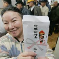 The envelope please: A woman holds up an envelope containing her cash handout Thursday at the municipal office in Nishimeya, Aomori Prefecture, one of two towns that began disbursing the money after the supplementary budget for 2009 cleared the Diet on Wednesday. | KYODO PHOTO
