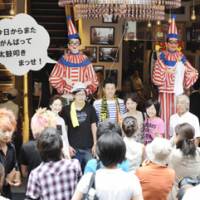 Back beat: Visitors have their picture taken in front of the mechanical drummer man Kuidaore Taro (left), which returned to Osaka\'s Dotonbori area Sunday, and his \"younger brother\" Kuidaore Jiro. | KYODO PHOTO