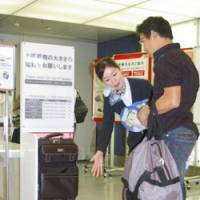 Travel light: A flight attendant shows a passenger Wednesday what the new size and weight limits for a carry-on bag will be when new baggage rules take effect at Haneda airport in Tokyo in December. | KYODO PHOTO