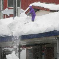 A man clears snow from the roof of a shopping arcade in Tokamachi, Niigata Prefecture, on Wednesday. A cold front has dumped heavy snow on extensive parts of Japan, killing at least 51 this winter. | KYODO PHOTO