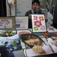 Drawn together: Maki Saito, secretary general of NGO JIM-NET, shows drawings by pediatric cancer patients in Iraq and photos of children from Fukushima Prefecture that are part of a Tokyo exhibit that started Wednesday. | KYODO