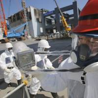Hazard pay: A worker at the Fukushima No. 1 nuclear complex gets a radiation reading of 114 microsieverts per hour on March 6 near reactor 4, which stands surrounded by cranes next to the concrete foundations for a storage facility for melted fuel rods. | POOL