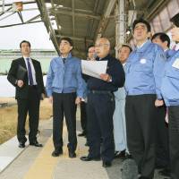 Standing still: Prime Minister Shinzo Abe (right) listens as Tomioka Mayor Katsuya Endo describes the damage to Tomioka Station in Fukushima Prefecture on Sunday. | POOL