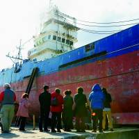 People on March 10 are dwarfed by the Kyotoku Maru No. 18, which was left stranded on a pier in Kesennuma, Miyagi Prefecture, by the March 11, 2011, tsunami. Officials said Monday the vessel will be dismantled in April. | KYODO