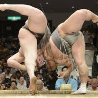 Going down: Hakuho (left) and Toyonoshima lean over the ring during their bout at the Summer Grand Sumo Tournament on Monday. Toyonoshima emerged the victor. | KYODO