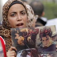 Fighting in the streets: An Egyptian woman participating in a protest rally against the ruling Muslim Brotherhood in Cairo on Saturday holds up a poster showing what she said are victims of Friday night\'s clashes in the Nile delta city of Mansoura. | AP