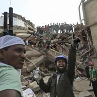 Amid the ruins: A Bangladeshi rescuer shouts for assistance as another waits with a stretcher to take away the injured or deceased Thursday at the site of a building that collapsed Wednesday in Savar, near Dhaka. | AP
