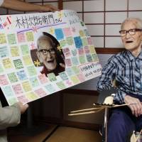 For record longevity: Jiroemon Kimura is offered a board with congratulatory messages from local elementary school pupils at his home in Kyotango, Kyoto Prefecture, in September. | CITY OF KYOTANGO/KYODO