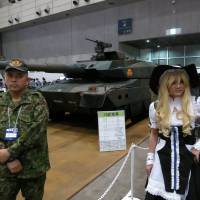 Real cyberworld: A \"cosplayer\" poses with a Ground Self-Defense Force member and its main battle tank during the Nico Nico Chokaigi event Saturday at Makuhari Messe in Chiba. | KAZUAKI NAGATA