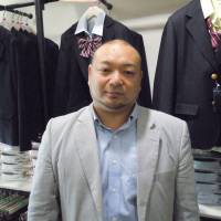 Takayuki Aiura, president of CONOMi, stands in front of racks of fake uniforms at his store in the Harajuku district of Tokyo in mid-April. | TOMOHIRO OSAKI