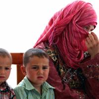 Temporary home: A newly arrived Syrian refugee woman covers her face as she sits on a bench with her children at the Mrajeeb al-Fhood refugee camp in Zarqa, Jordan, on Monday. | AP