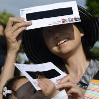 Mother and child take view the eclipse with homemade eclipse viewers. | KYODO