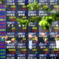 Wild ride: Passersby are reflected on a board of the Tokyo Stock Exchange on Friday as the Nikkei 225 ended higher despite swinging by over 1,000 points, with a sound U.S. economic outlook prompting buying and a firmer yen spurring sales. | AFP-JIJI