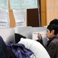 Check the fine print: A resident of Minato Ward, Tokyo, checks her ballot Sunday at a local polling station. | SATOKO KAWASAKI