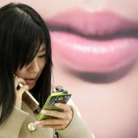 Easy target: A woman talks on her mobile phone while checking her smartphone in Tokyo in April. | BLOOMBERG