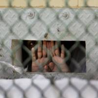 A detainee shields his face as he peers through the cell door opening used to pass food and other items to detainees. U.S. President Barack Obama has renewed his call to shut the facility. | AP