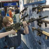 A young man who chose not to give his name sizes up an assault rifle during the annual convention a day earlier. The rifleman: behind assault weapons' rise