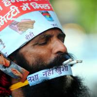 Puffing away: Rajendra Kumar Tiwari, a performer, smokes two cigarettes at  the same time as he campaigns with a magician during World No Tobacco Day in Allahabad on Friday. | AFP-JIJI