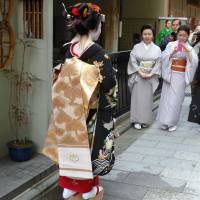 Maiko Ko-ume\'s house mother- tutor, famed ex-geisha Koito, stands demurely with hands clasped regarding her proudly. | LESLEY DOWNER PHOTO