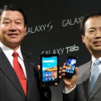 Into the galaxy: DoCoMo President Ryuji Yamada (left) and J.K. Shin, president and head of the mobile communications business at Samsung, show off the new Galaxy Tab and the Galaxy S smart phone at a press conference Tuesday. | KAZUAKI NAGATA PHOTO