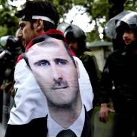 A Syrian man wrapped in a national flag with a portrait of President Bashar Assad walks past riot police during an anti-Israel demonstration in Tehran on May 6. | AP
