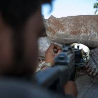 Under the gun: A Syrian rebel fighter points his rifle through a hole in sandbags as he holds a position in a trench 100 meters from the regime-controlled Wadi Deif military base in the village of Kfarruma on Friday. | AFP-JIJI