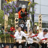 Popular \"enka\" singer Hiroshi Itsuki (left) dons a happi coat and boards a float to take part in the Hakata Gion Yamakasa festival in Fukuoka on Saturday. Several colorfully decorated, 1-ton floats raced through the streets of Hakata the same day for the annual summer event, which runs through Monday. | KYODO