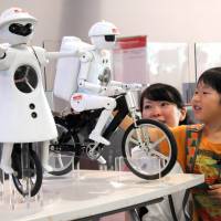 All bot balance: Nagi Machino, 5, checks out Murata Manufacturing Ltd.\'s bike-riding robot Murata Seisaku-kun as a guide gives him an explanation Thursday at the National Museum of Emerging Science and Innovation in Koto Ward, Tokyo. The Kyoto-based firm\'s unicyclist robot, Murata Seiko-chan, is also on exhibit until Aug. 4. | SATOKO KAWASAKI
