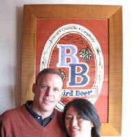 Bryan and Sayuri Baird pose in front of the Baird Beer logo at The Fishmarket Taproom in Numazu, Shizuoka Prefecture. | KRIS KOSAKA PHOTO