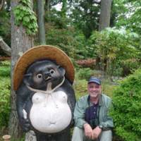 A fine pair: The author (right) sits beside a stately  tanuki  (raccoon dog) statue at secluded Komponji Temple. | MARK BRAZIL PHOTOS