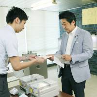 Early bird: Prime Minister Shinzo Abe hands an absentee ballot for Sunday\'s Upper House election to an official in Shibuya Ward, Tokyo, on Tuesday. | POOL
